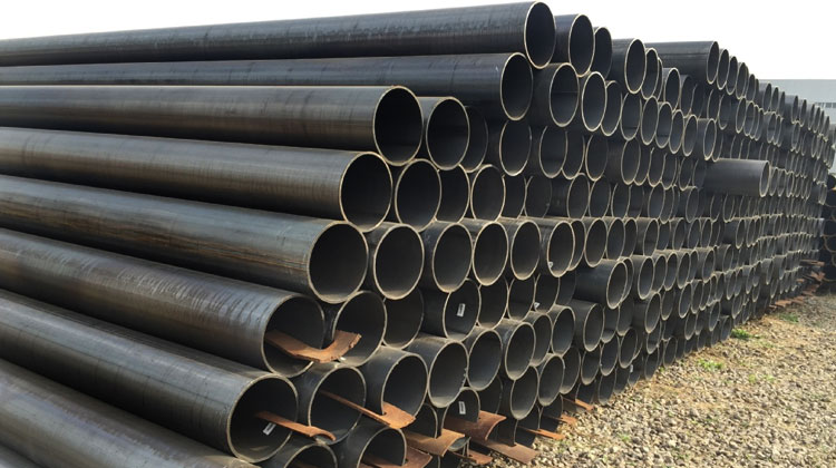 Large black steel pipes stacked outdoors in rows.